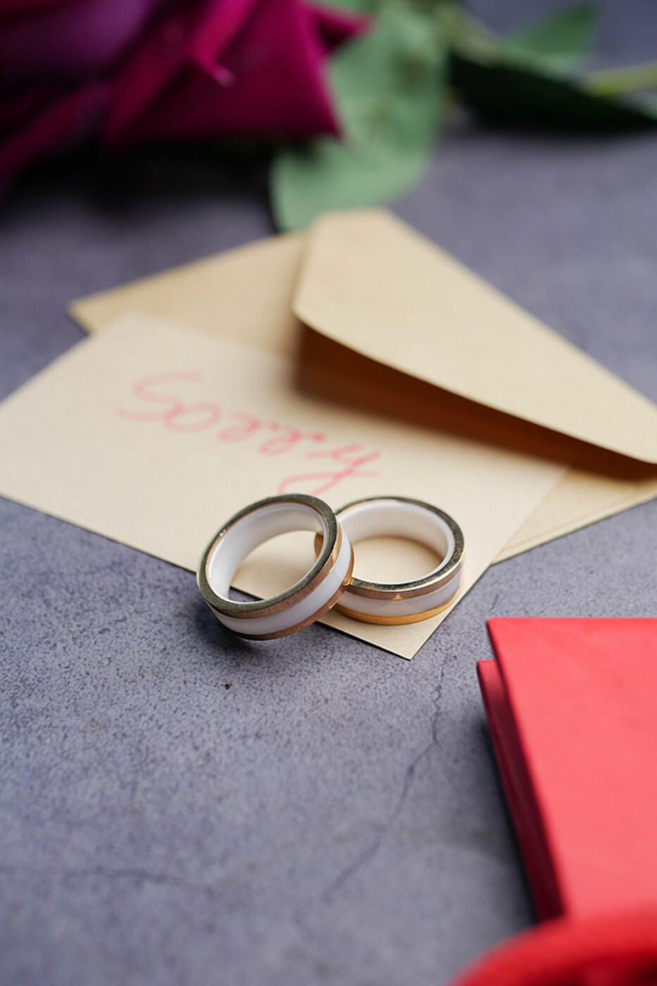 a pair of wedding rings next to an envelope that says "sorry."