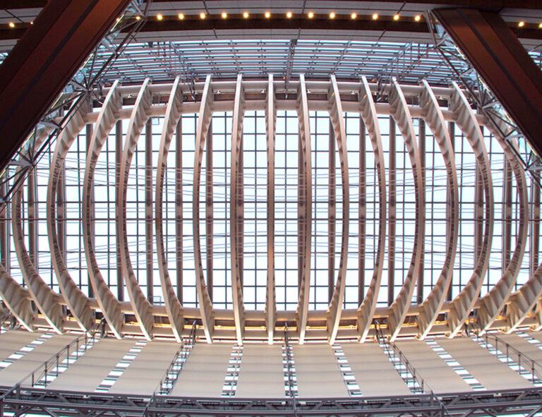 Image from below of a modern architecture building with numerous arches against glass.